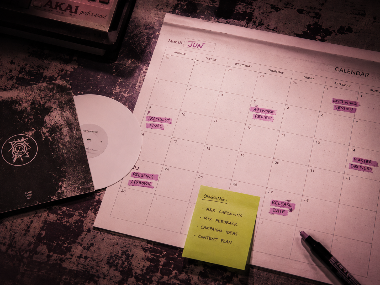 Calendar page with marked dates in mauve highlighter, lime sticky note, small reference vinyl, vintage industrial desk